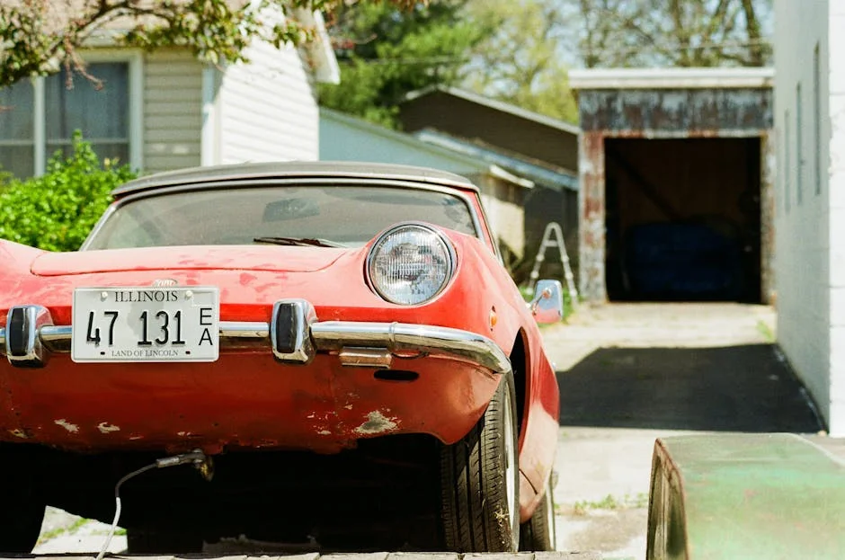 A vintage red car with an Illinois license plate parked in a residential driveway. - best affordable project cars for beginners