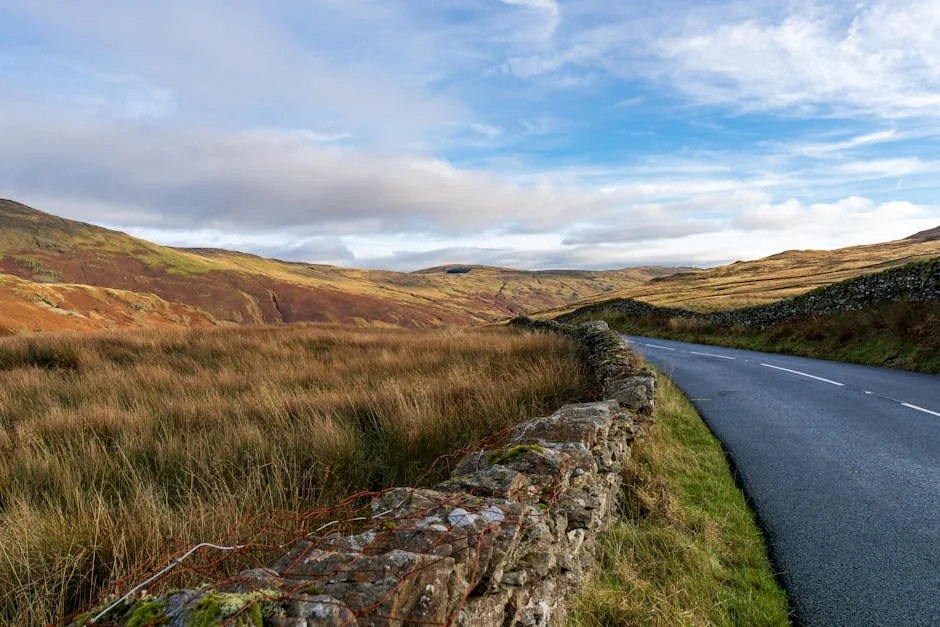 Beautiful winding road through a picturesque countryside landscape with stone walls under a clear sky. - best driving roads in the united kingdom