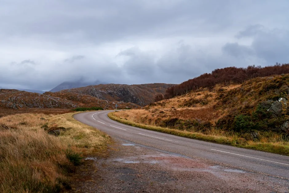 Scenic view of a winding road through the autumn-colored Scottish Highlands under a cloudy sky. - best driving roads in the united kingdom
