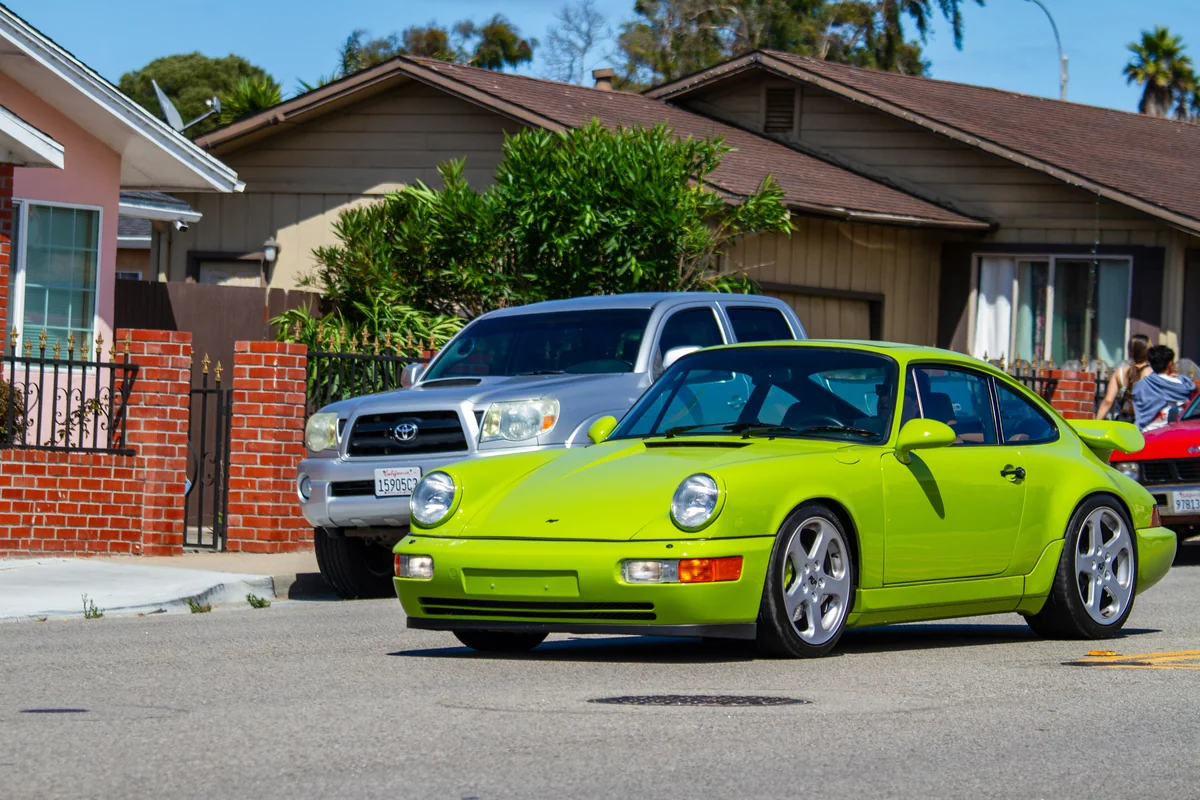 A bright green porsche drives down a suburban street. - most popular car meets in california