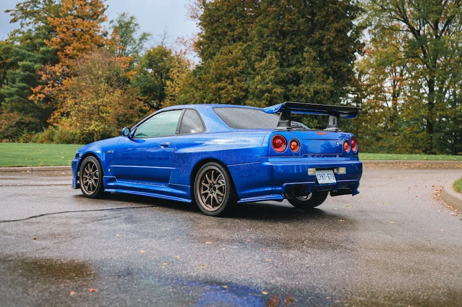 A vibrant blue Nissan Skyline GT-R parked on a wet road surrounded by autumn foliage. - underrated jdm cars under 10k